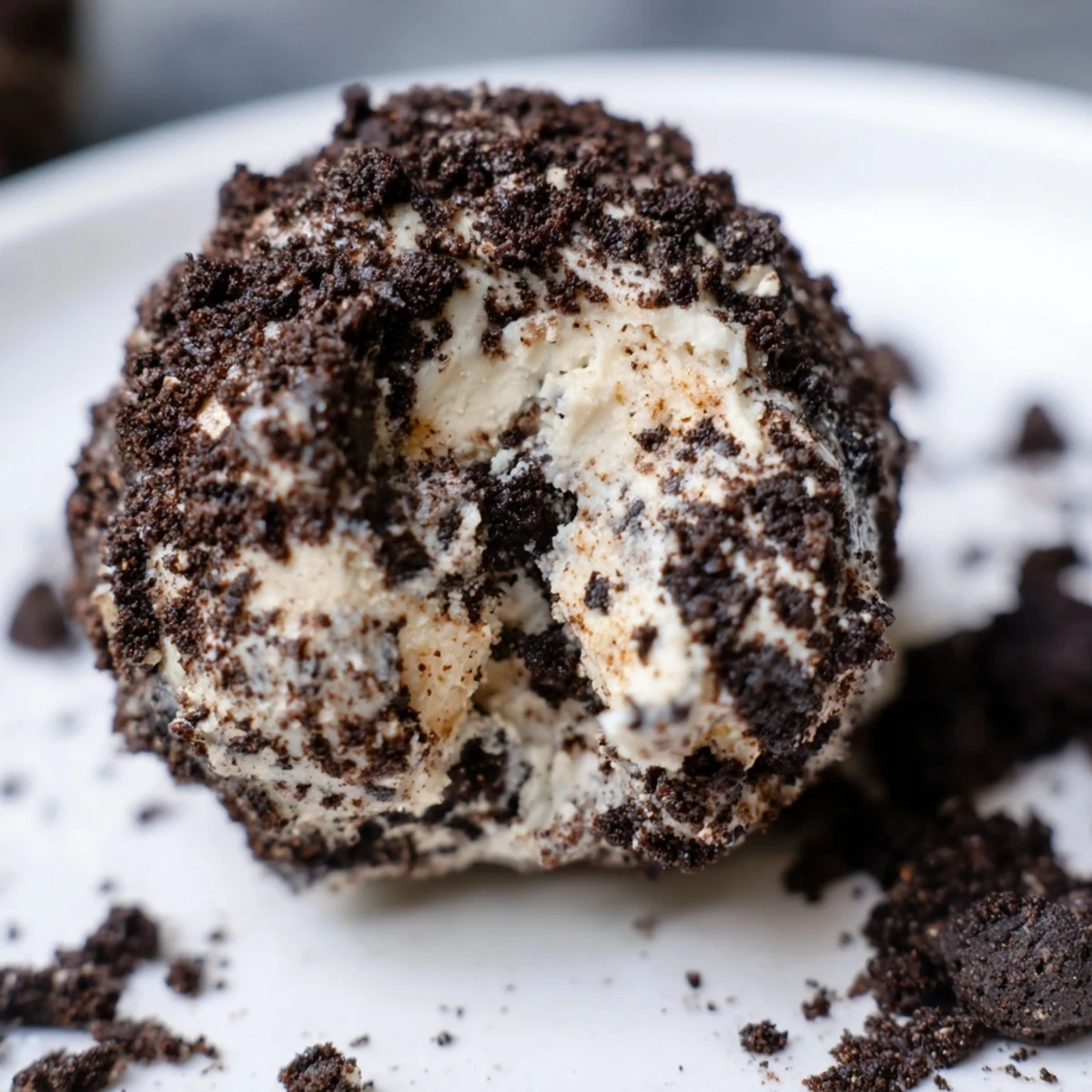 Cream Cheese Oreo Protein Balls rolled in dark cookie crumbs with chocolate drizzle on white plate