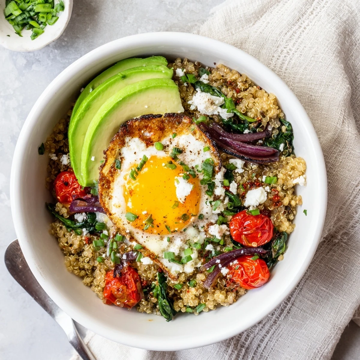 Golden fried egg resting atop fluffy quinoa breakfast bowl with colorful sautéed vegetables
