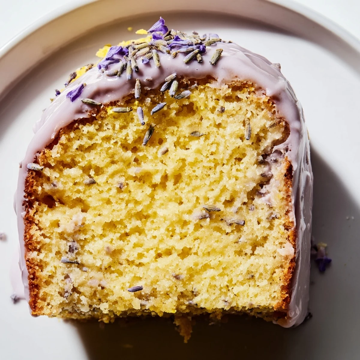 Lavender cake with lemon glaze drizzled over a tender crumb, garnished with purple buds