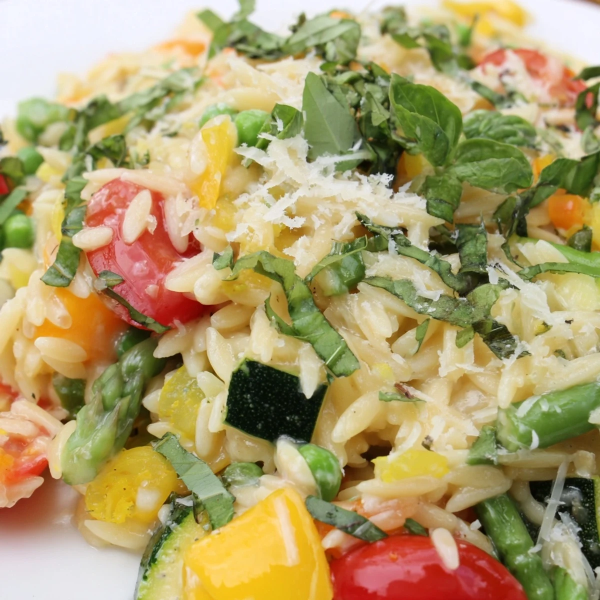 Creamy Orzo Primavera with colorful vegetables in a skillet garnished with fresh basil
