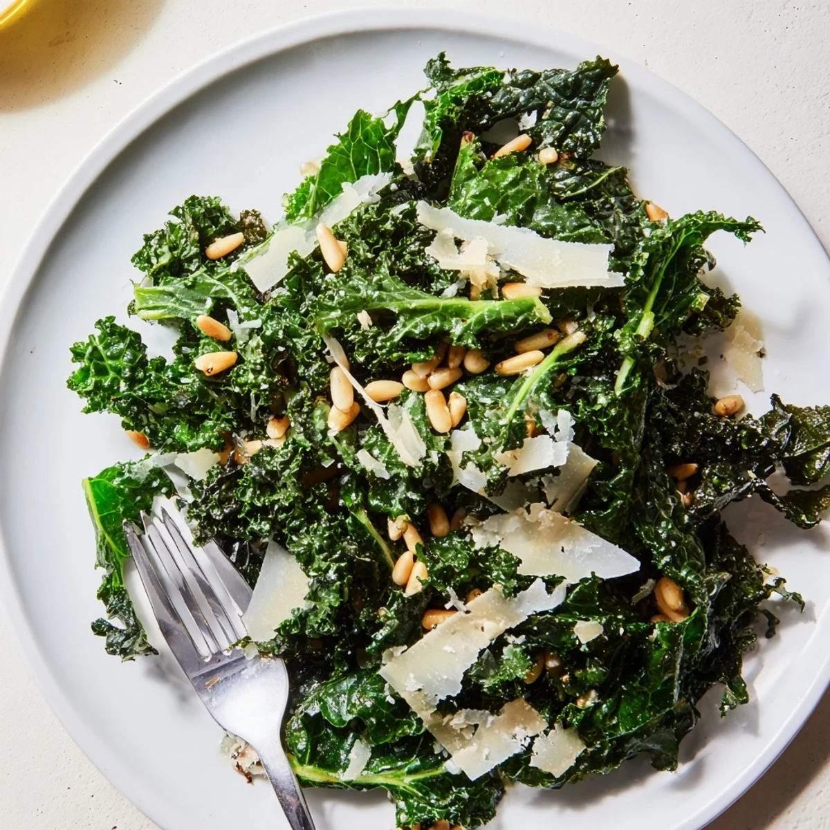 Garlic lemon Parmesan kale salad topped with shaved cheese and toasted pine nuts