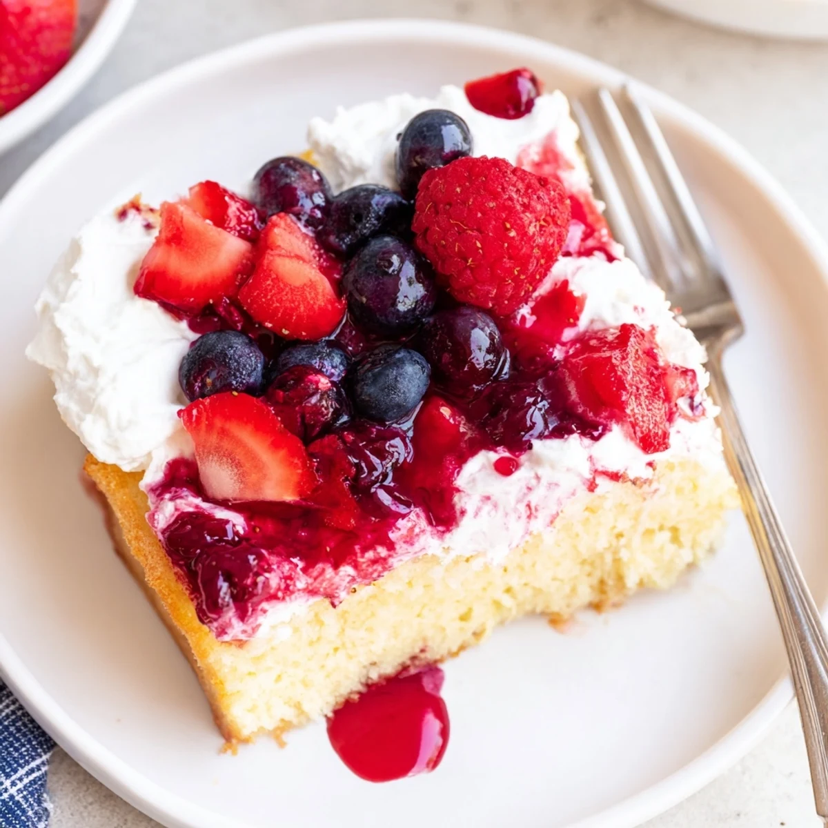 Chilled Summer Berry Poke Cake crowned with fresh berries, light cream, hint of lemon