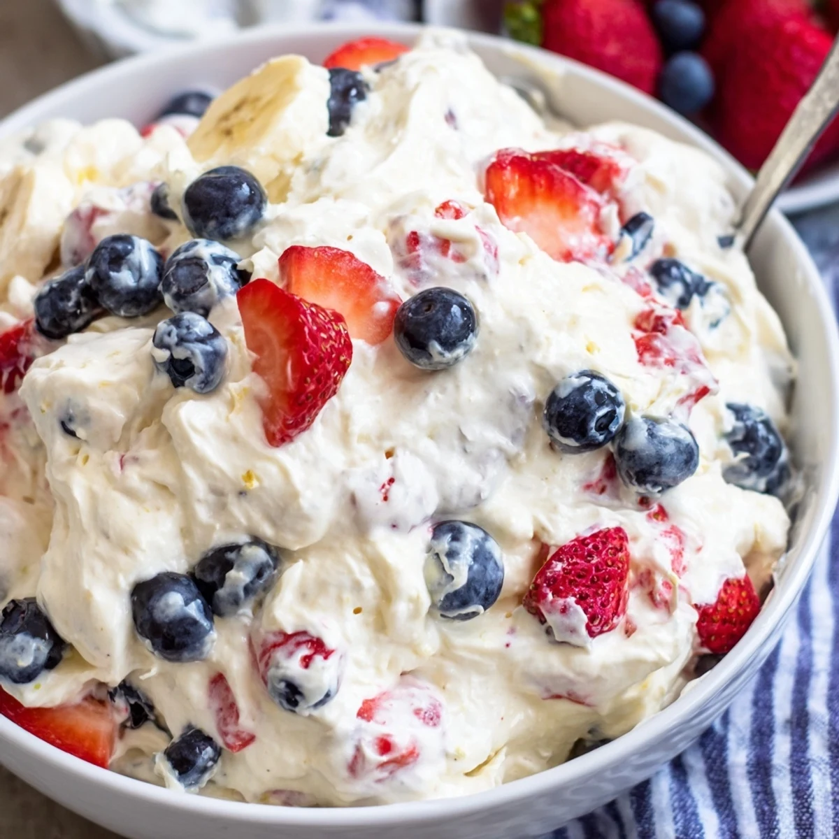 A spoonful of Red White And Blue Cheesecake Salad garnished with extra blueberries