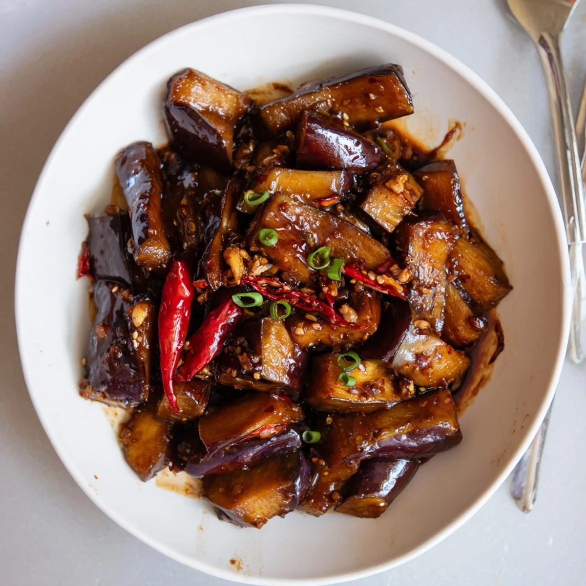 Plate of Sichuan Style Braised Aubergines topped with scallions, steam rising