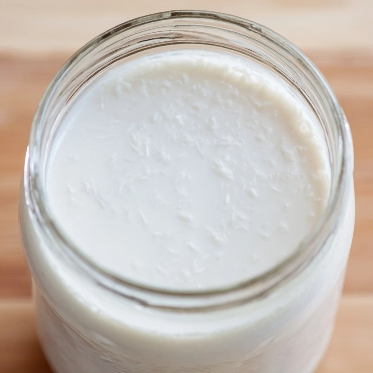 Creamy white homemade coconut milk being poured from blender into clear glass container