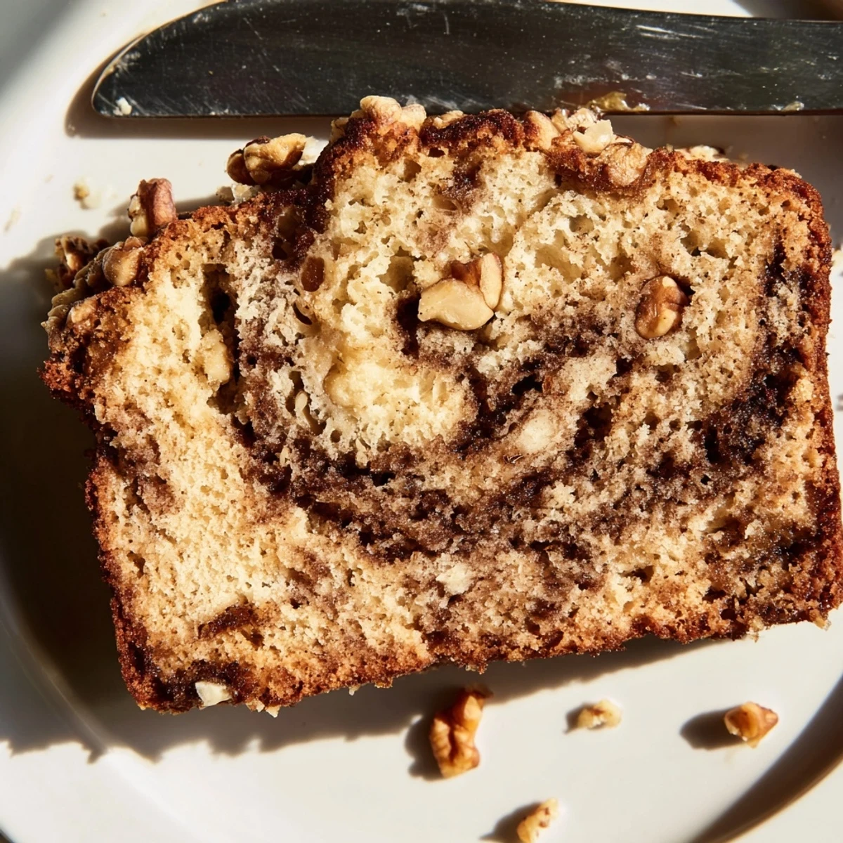 Sliced moist banana bread revealing cinnamon sugar layers and crunchy walnuts, served warm on a rustic wooden board