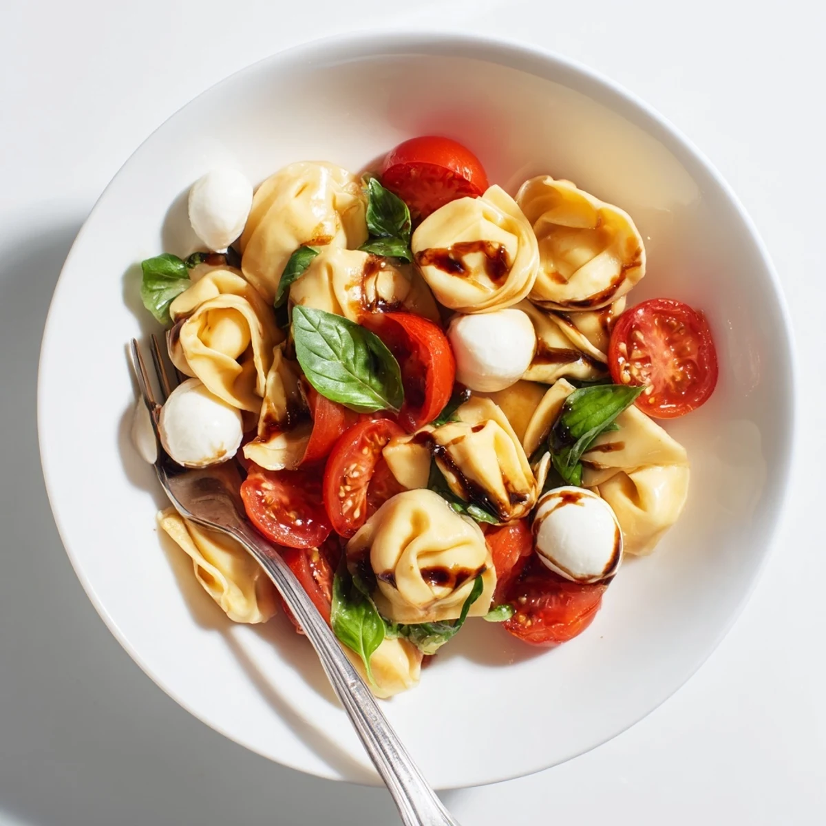 Colorful tortellini Caprese salad with cherry tomatoes, mozzarella balls, and fresh basil leaves in a white serving bowl