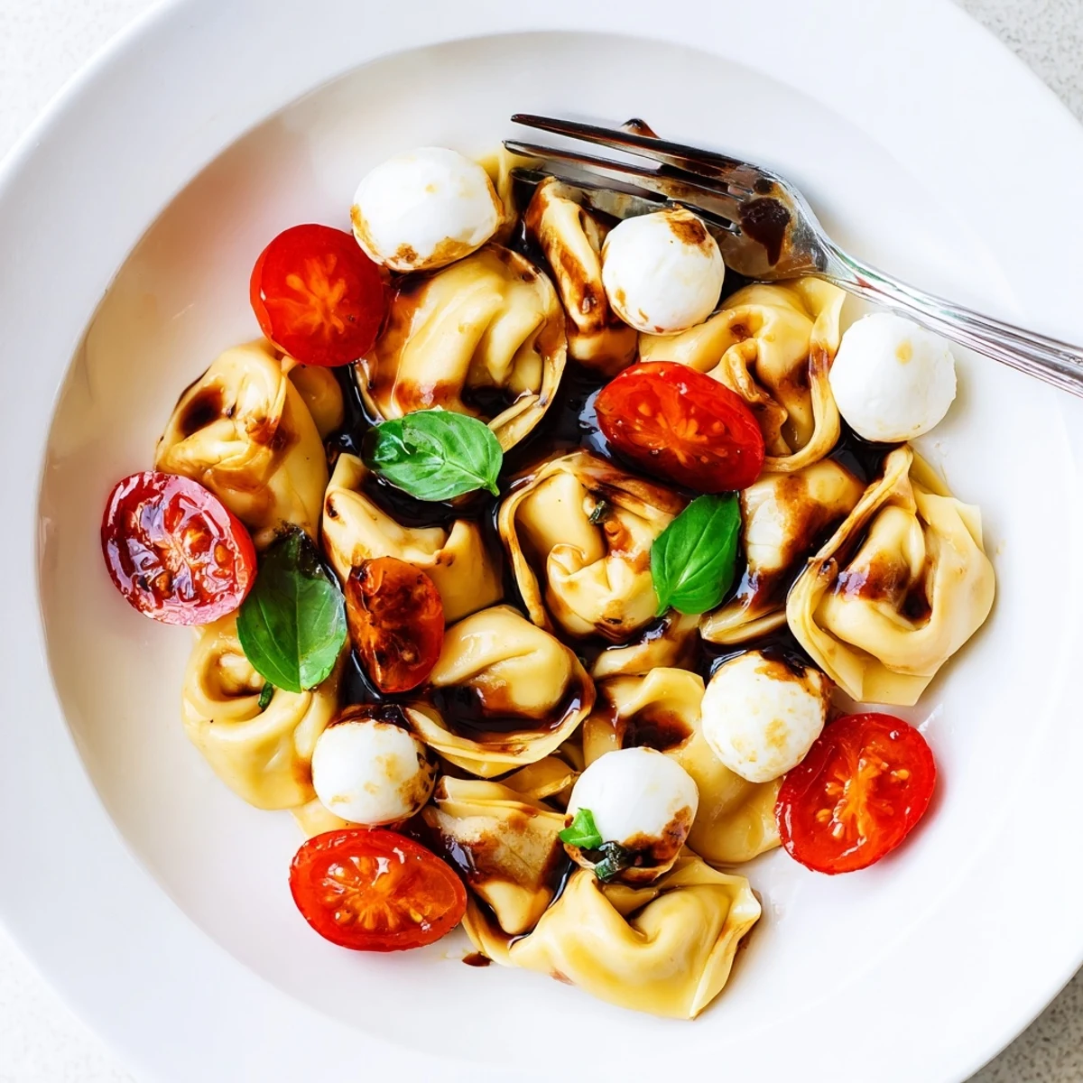 Italian-inspired tortellini Caprese salad featuring tender cheese pasta, juicy tomatoes, and torn basil in a glass mixing bowl