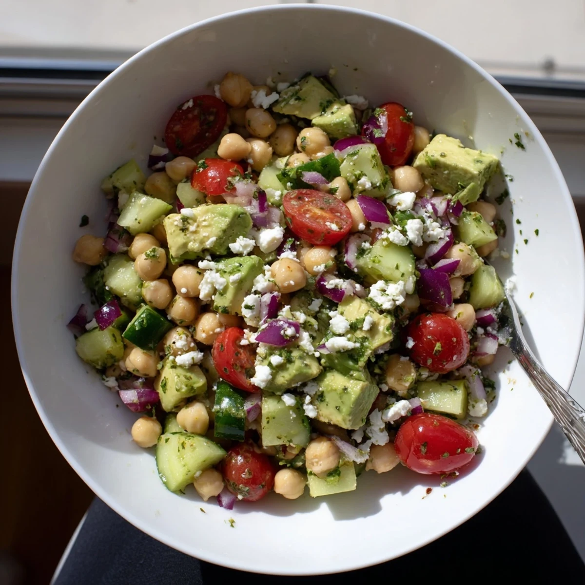 Vibrant chickpea feta avocado salad drizzled with lemon dressing in a wooden bowl
