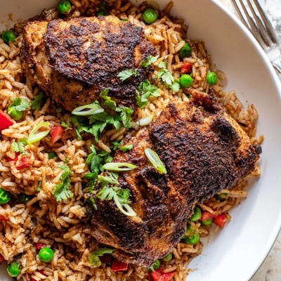 Golden brown jerk seasoned chicken thighs nestled in fragrant coconut rice with diced bell peppers